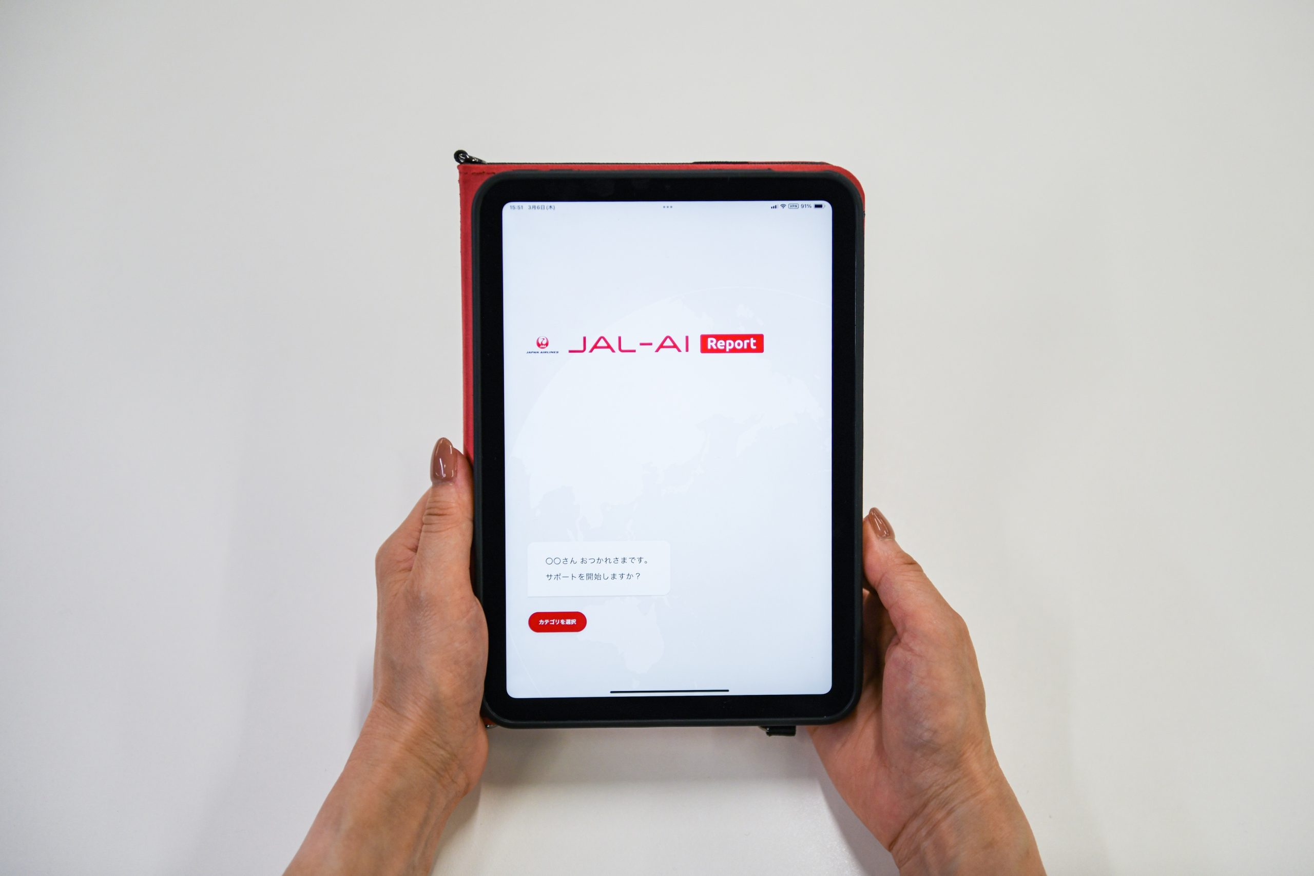 スクリーンにJAL-AI Reportアプリが表示されたタブレット端末を両手で持っている