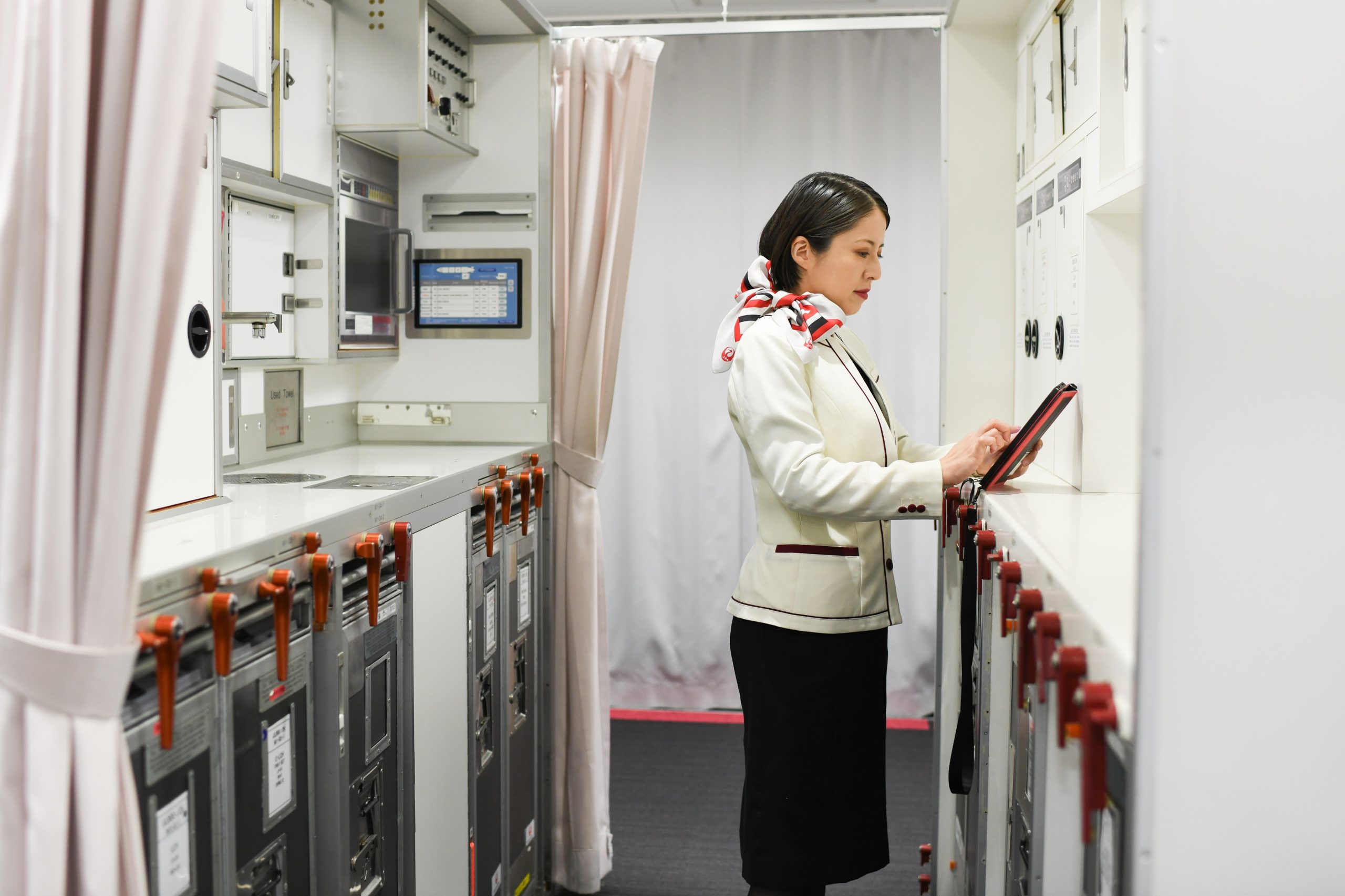 客室乗務員の制服を着た女性が、飛行機内ギャレーでタブレット端末を操作している