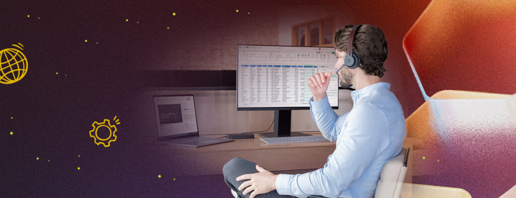 A man sits at a desk with a headset on looking at a laptop and a monitor; colorful background with shapes