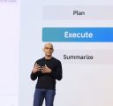 A bespeckled man in a black sweater stands in front of a large screen that reads, “Plan, Execute, Summarize.”