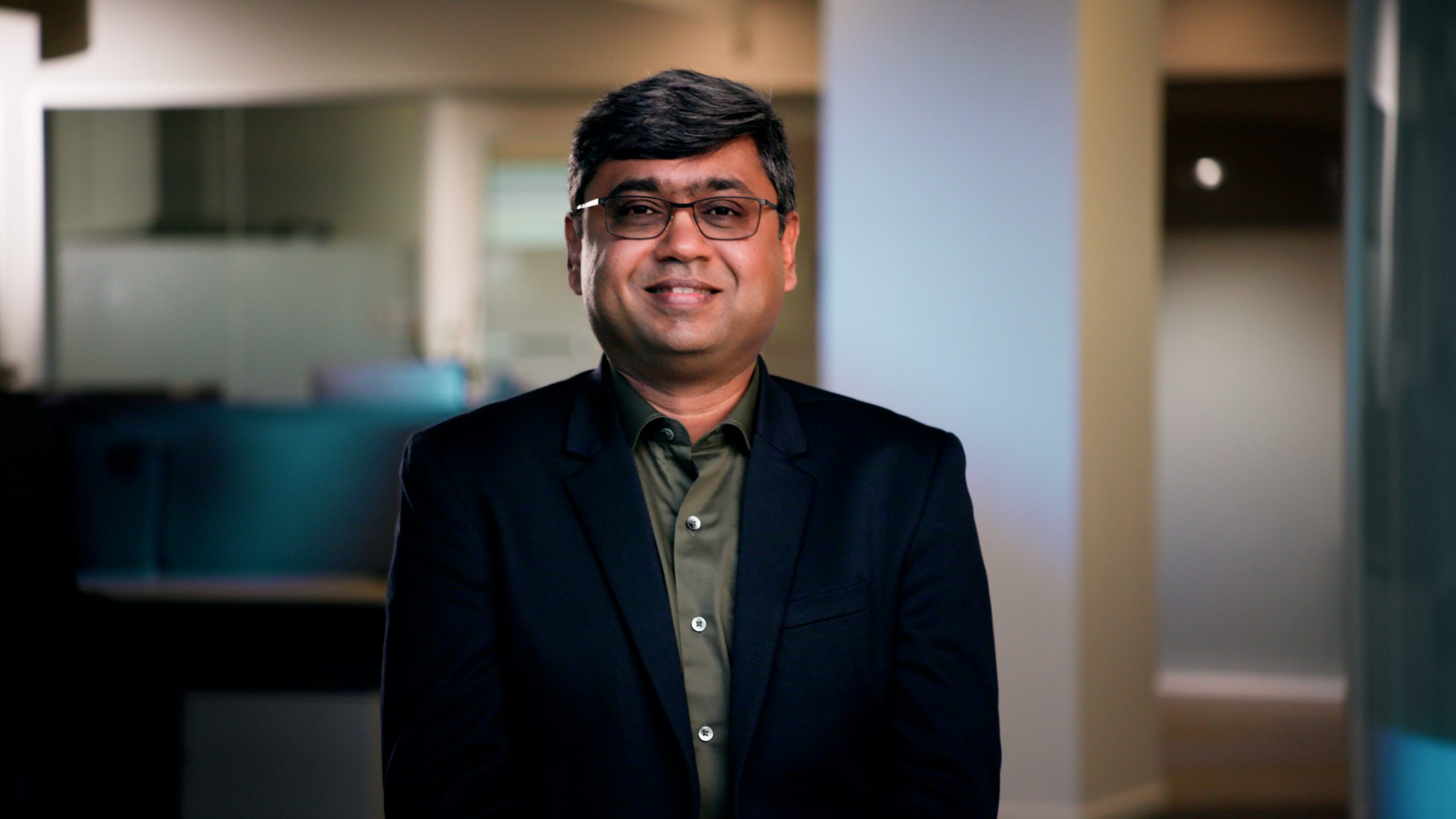 A man staring with glasses and a suit looking at the camera and smiling.