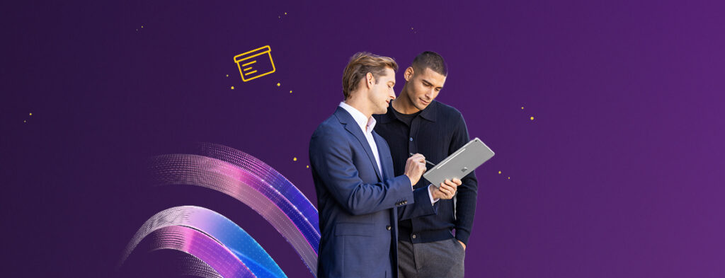 Two men look at a tablet PC together, on a background of colorful shapes.