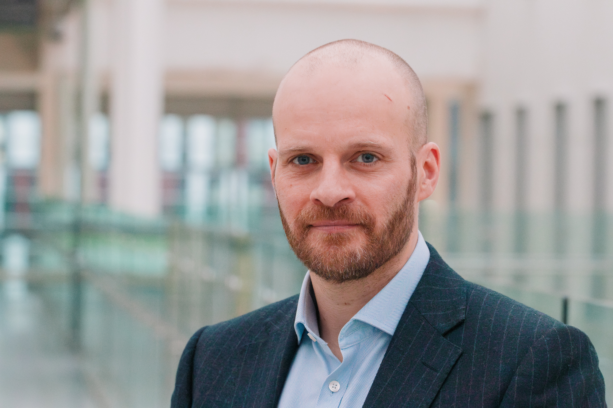 Portrait of a blue-eyed man in a light-filled corridor that is out of focus.
