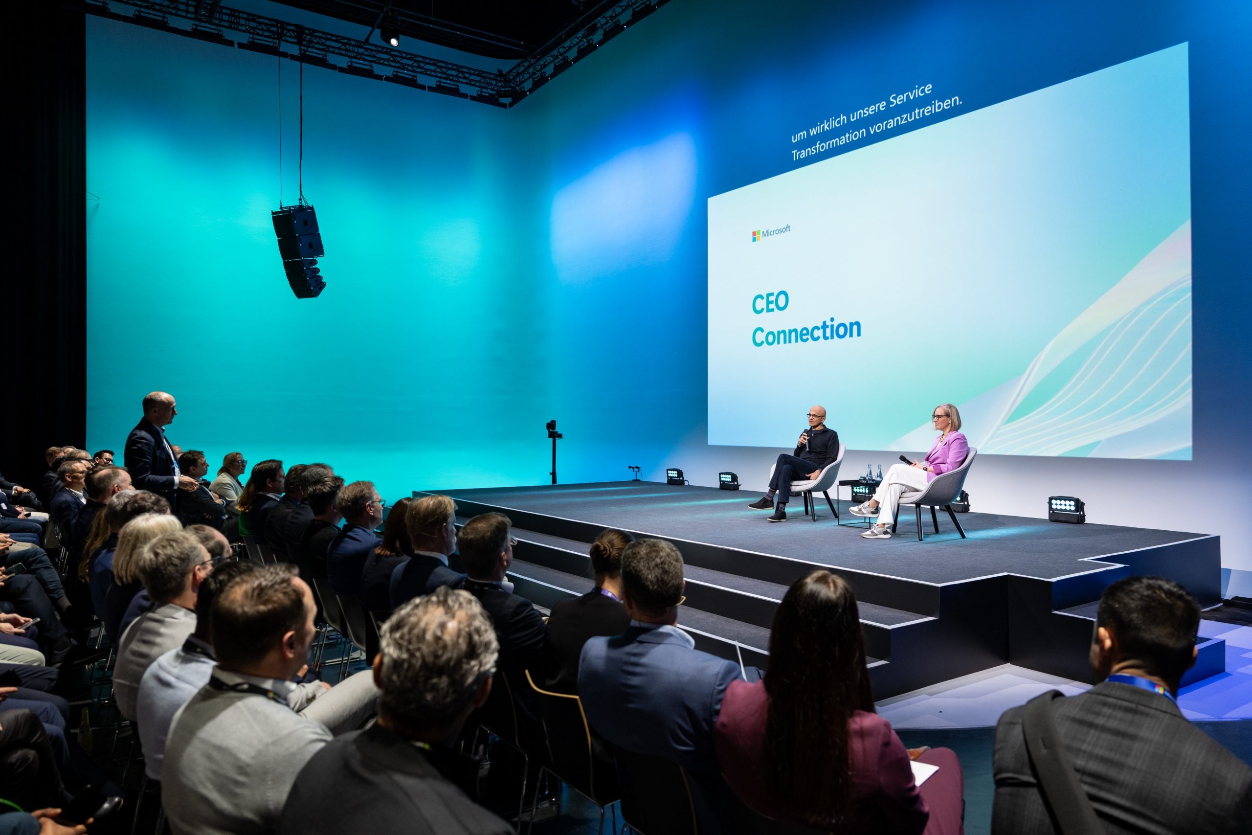 Zwei Sprecher im Gespräch auf der Bühne vor großem Publikum; auf der Leinwand steht „CEO Connection“ im Microsoft-Design.