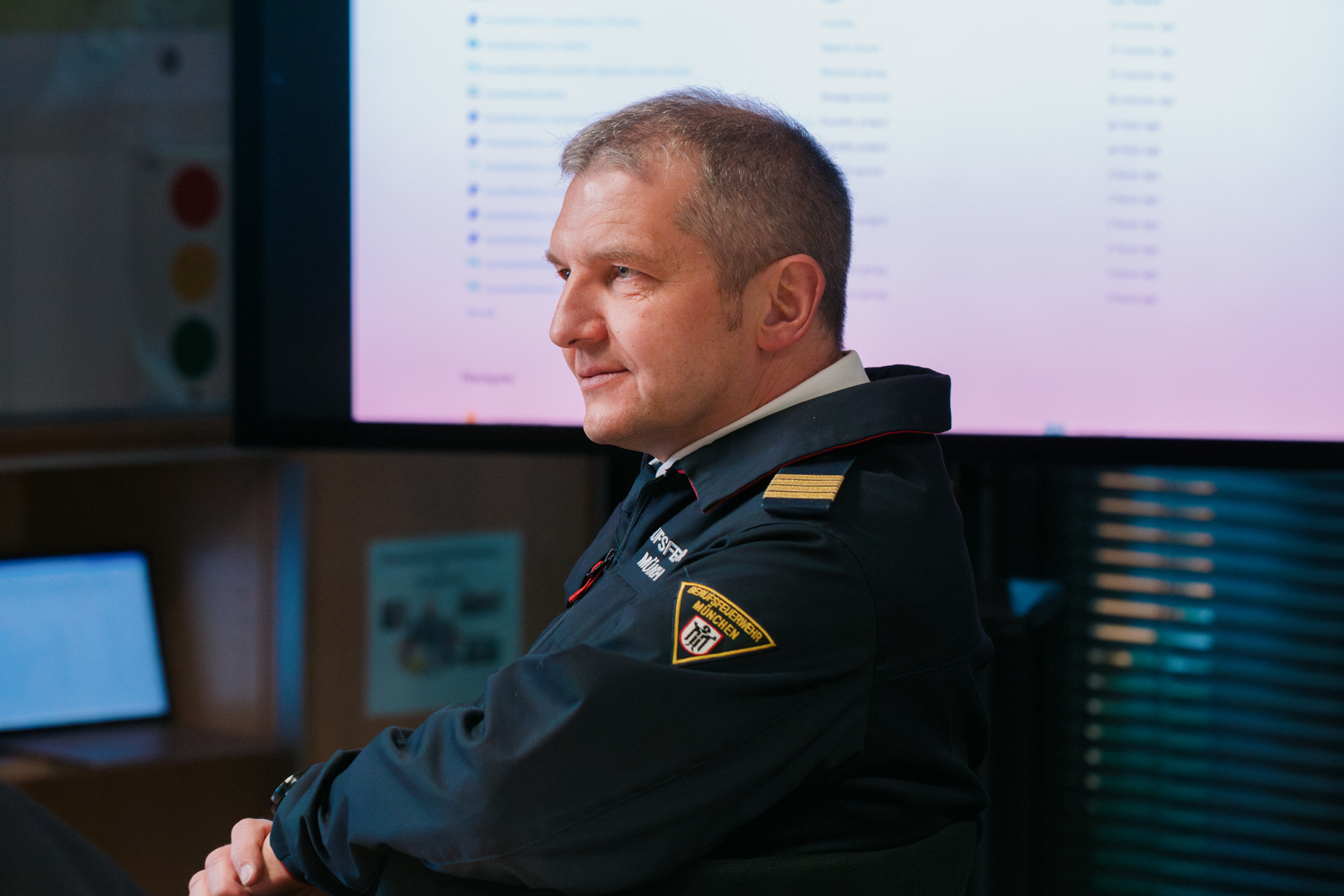 Porträt eines Mannes mit grauen Haaren in blauer Uniform vor Computerbildschirmen.