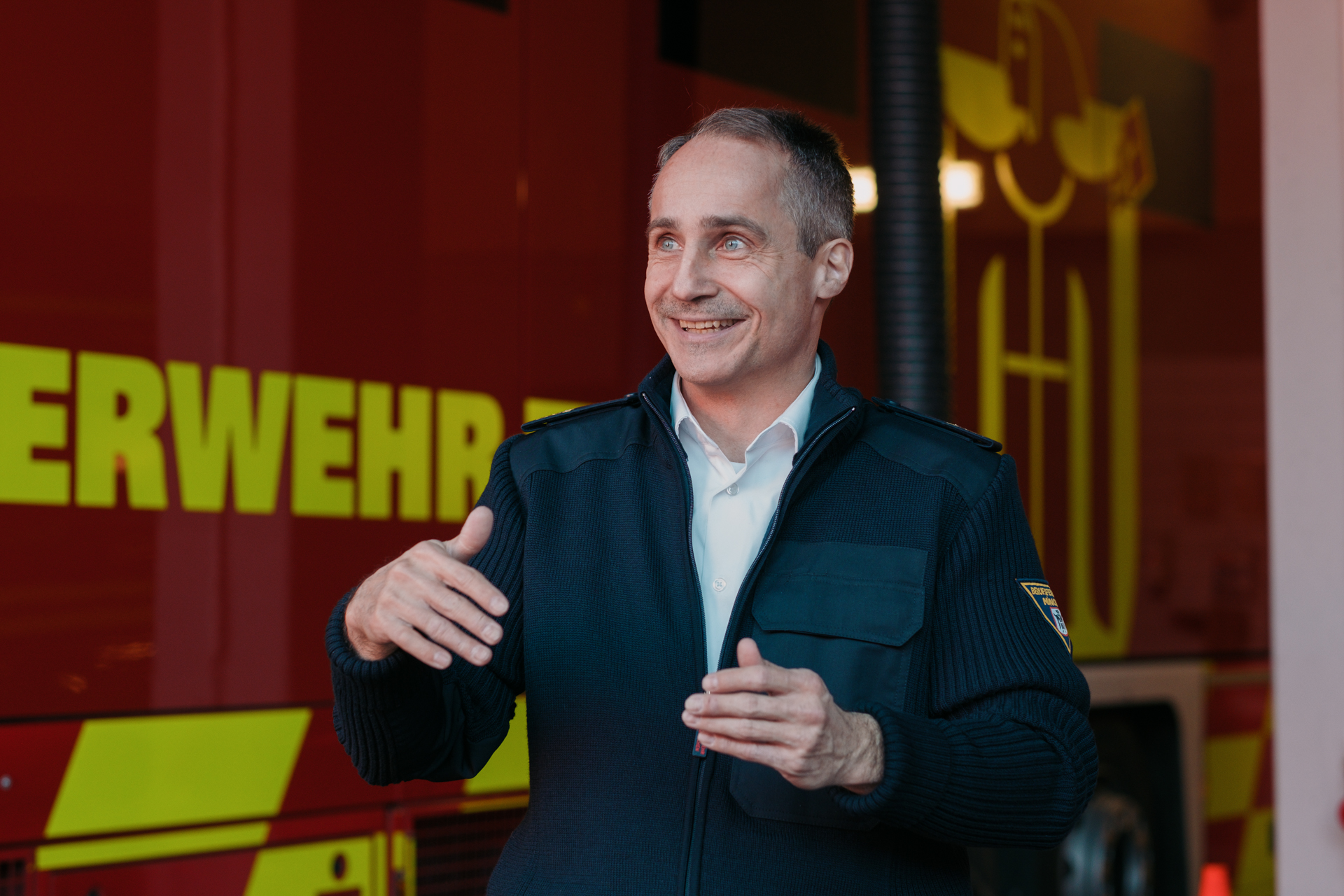 Mann in blauer Uniform vor einem Einsatzfahrzeug der Feuerwehr.