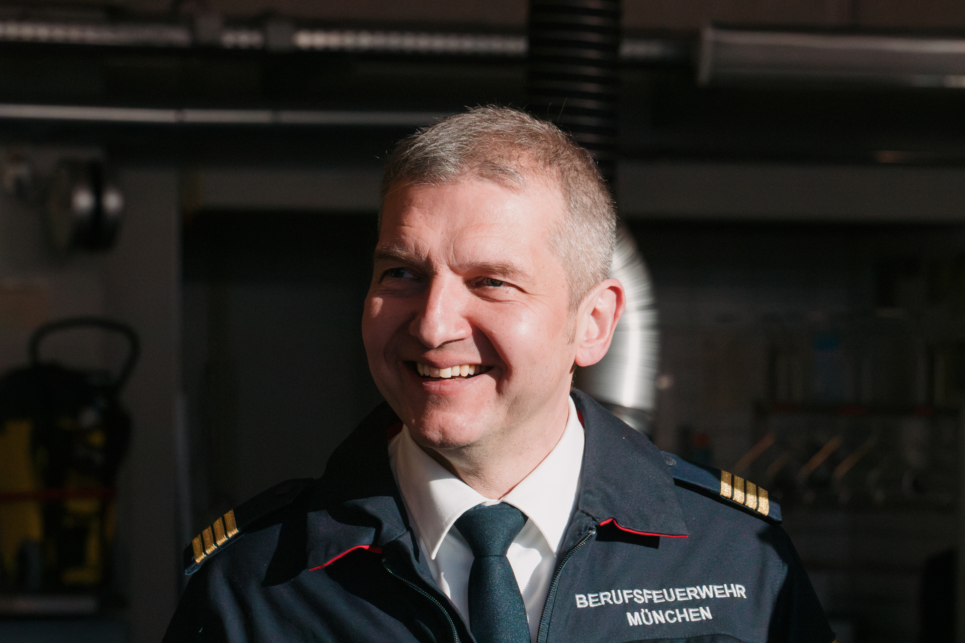Porträt eines lächelnden Mannes mit grauen Haaren in blauer Uniform vor Computerbildschirmen.