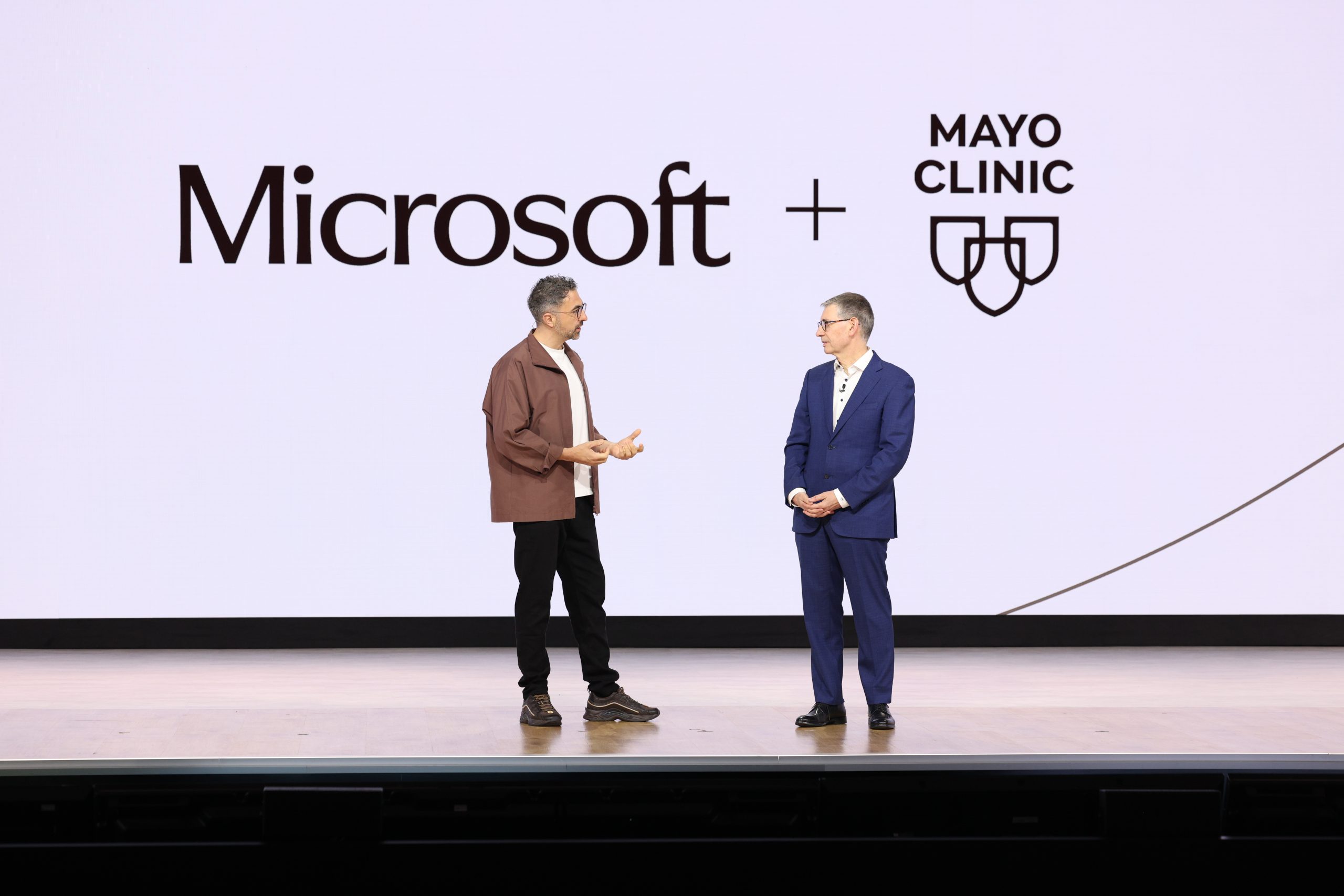 Two men stand on a stage having a conversation in front of a crowd
