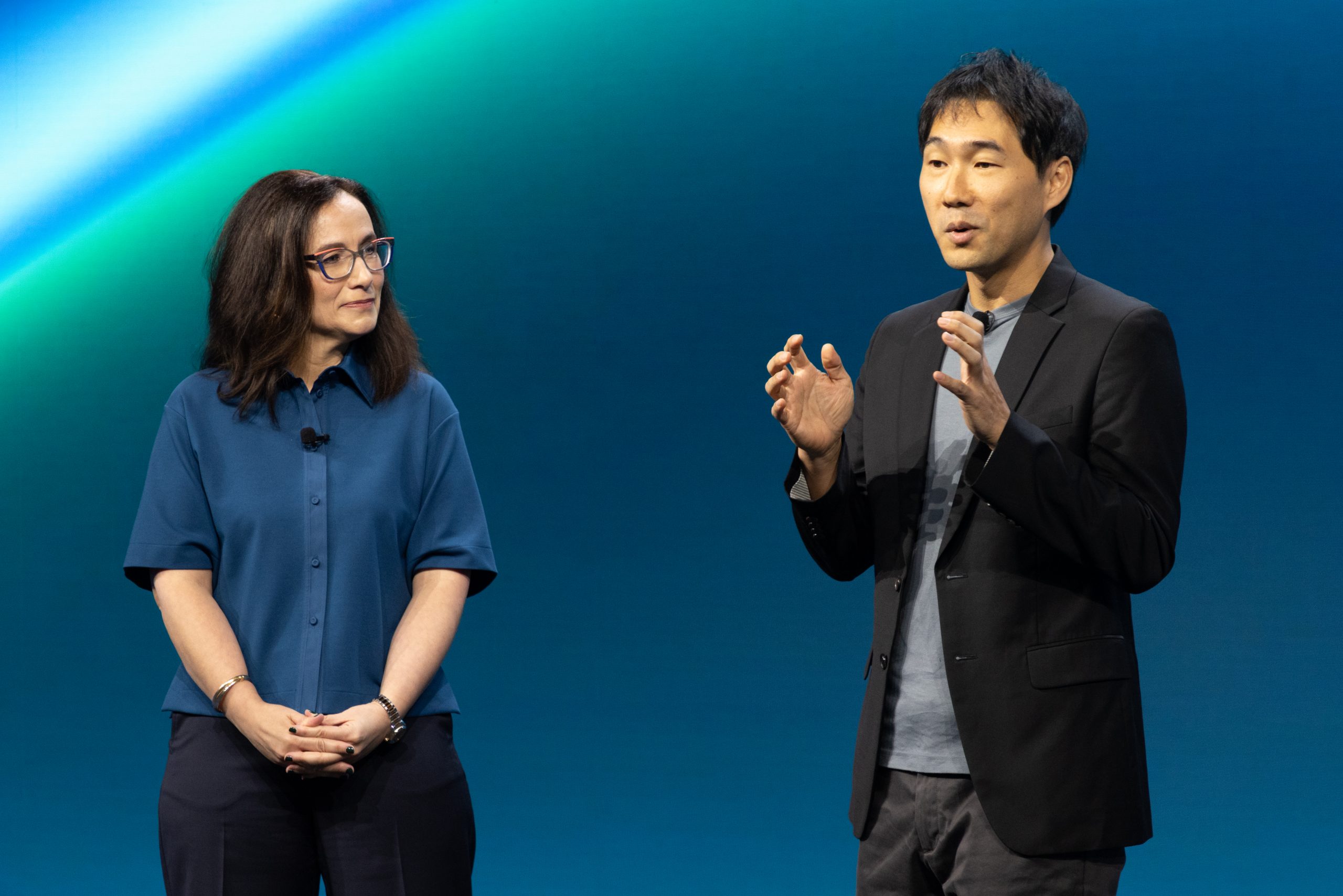 A man and a woman speak onstage during a presentation.